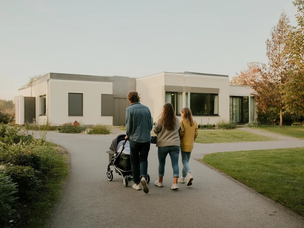 Young family with a pram in front of a bright single-family home, symbolic image for mortgages during parental leave